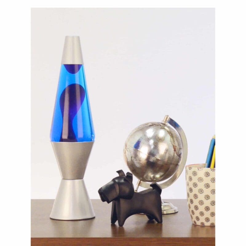 21180401US-LavaLamp-14-5-Purple-and-Blue-Lifestyle-web 14.5” LAVA® Lamp – Purple/Blue/Silver on table with scotty dog figure, silver globe, and a pencil cup